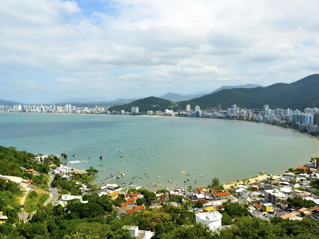 Enseada de Itapema vista do Mirante do Encanto: baía de água verde, orla de prédios e morros ao fundo