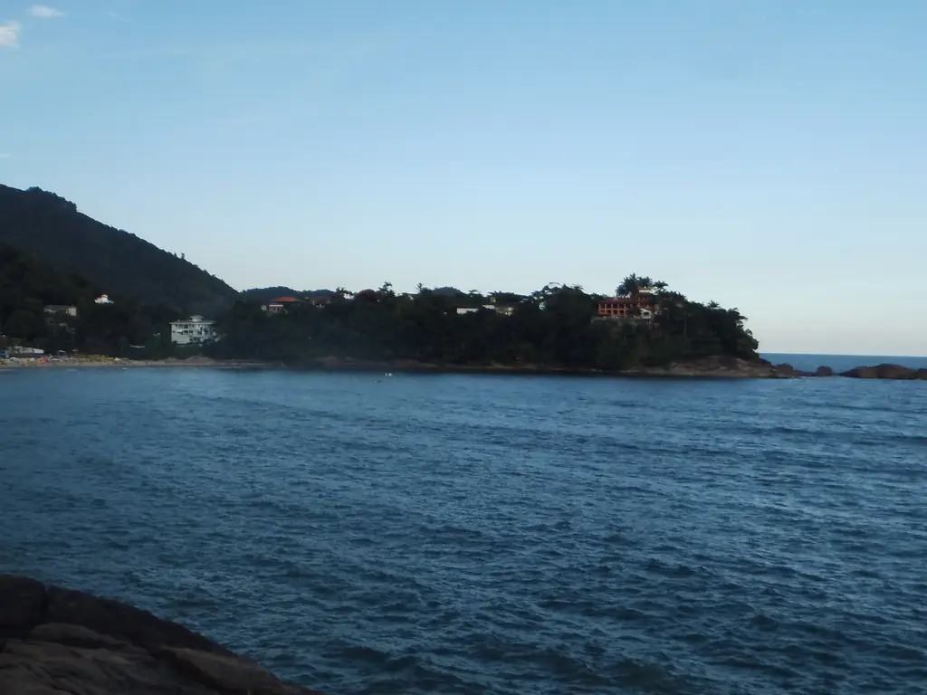 Praia do Tenório, em Ubatuba: mar azul, costão de pedra e morro coberto de mata sob céu limpo